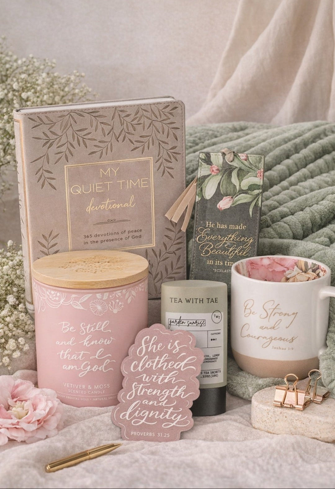 Collection of motivational items including a mug, candle, and book on a soft surface with flowers and a blanket.